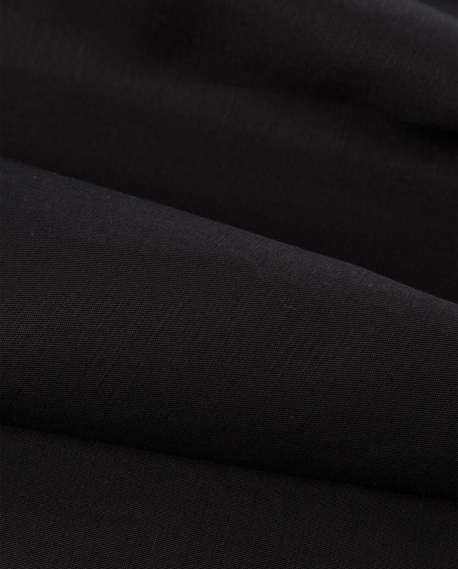 Close-up of the MANILA Dress by IVY OAK shows its smooth, black linen blend fabric with gentle folds and a slightly matte texture.