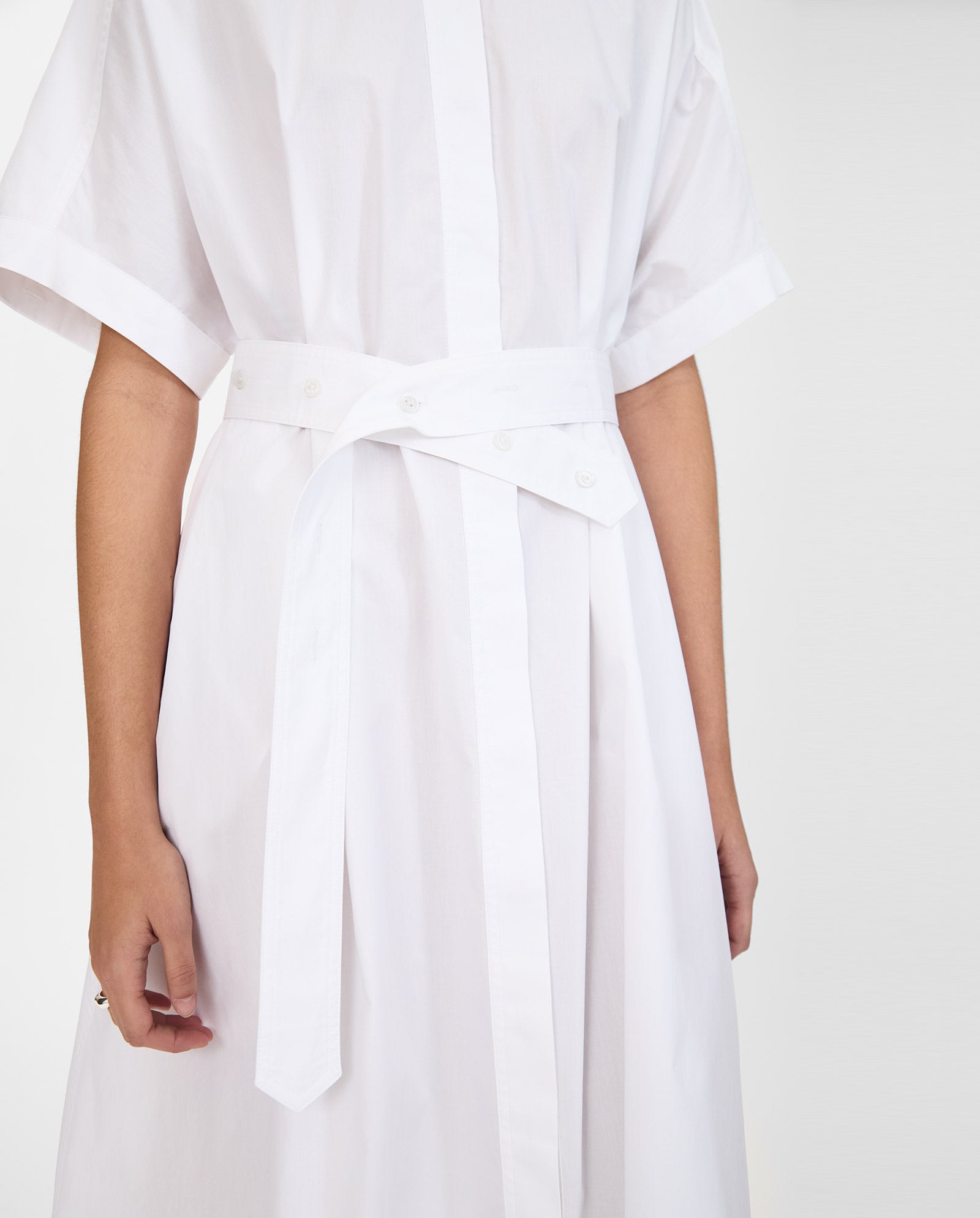A model wears the IVY OAK NORENA Dress, a white beach dress with short sleeves and a belted waist, shown from shoulders to knees for an effortlessly chic look.
