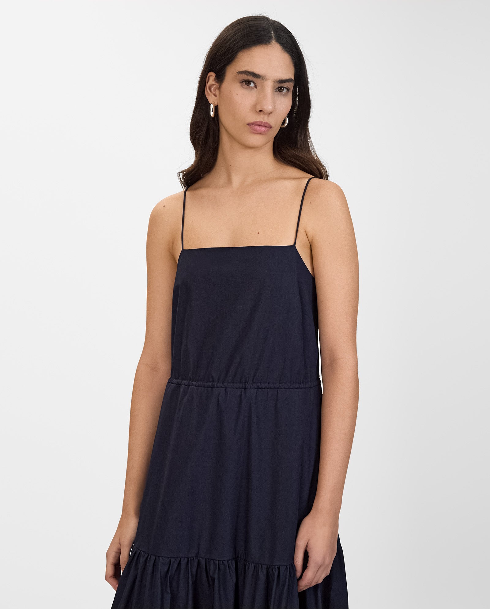A woman wears the IVY OAK NICOLINA Dress, a sleeveless dark navy maxi with adjustable straps, standing against a plain white background.