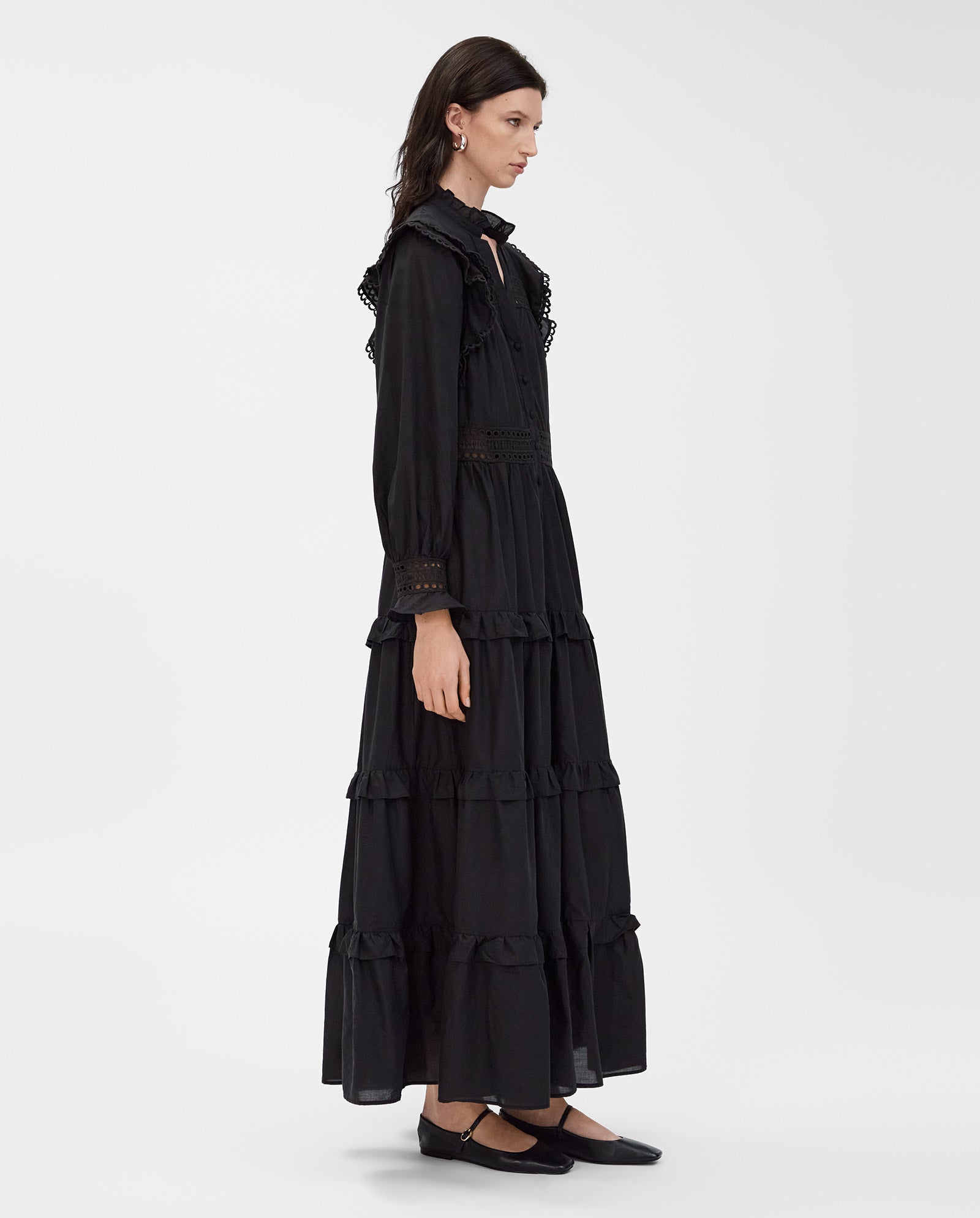 Woman in a long, black IVY OAK DENISA Dress made from cotton voile with lace tape applications, shown in profile against a plain background.