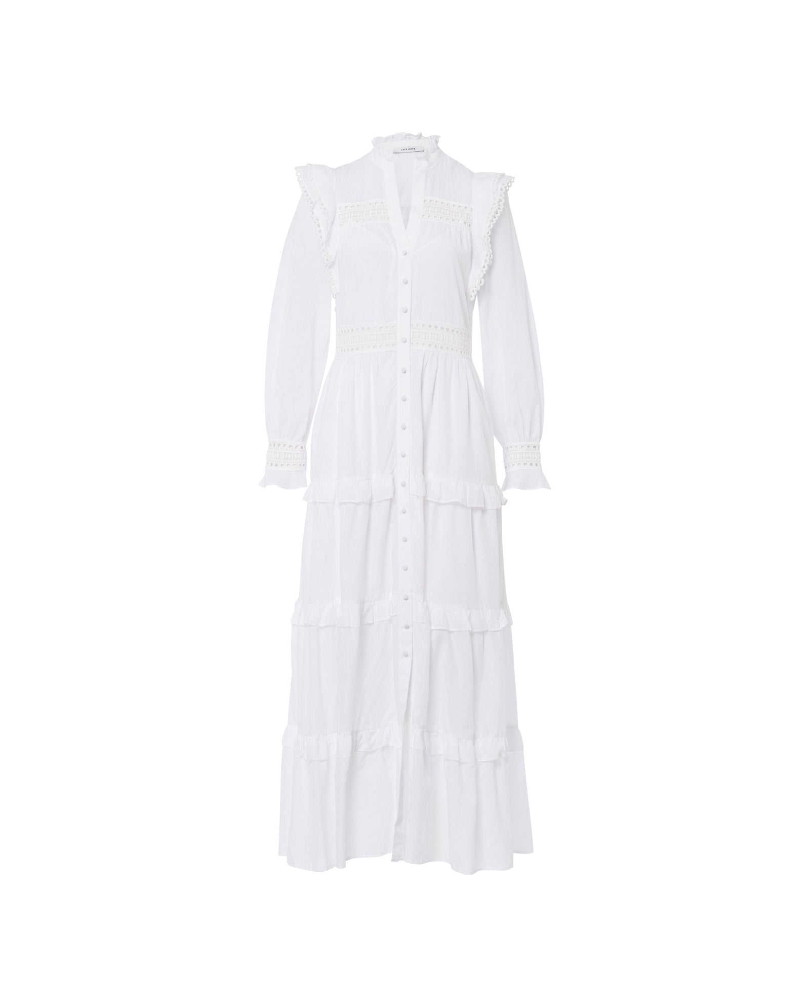 The IVY OAK DENISA Dress is a long white cotton voile dress with fabric-covered buttons, ruffled trim, lace tape details, long sleeves, and a tiered skirt, shown on a white background.