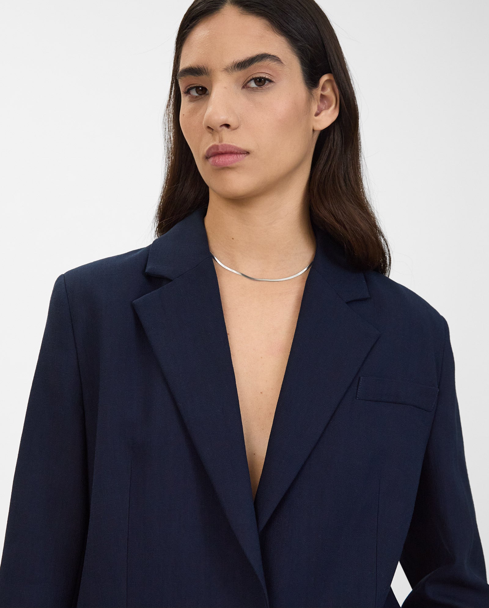 Person with long dark hair wears the IVY OAK JUNA Blazer with matching trousers, paired with a simple silver necklace, looking at the camera.