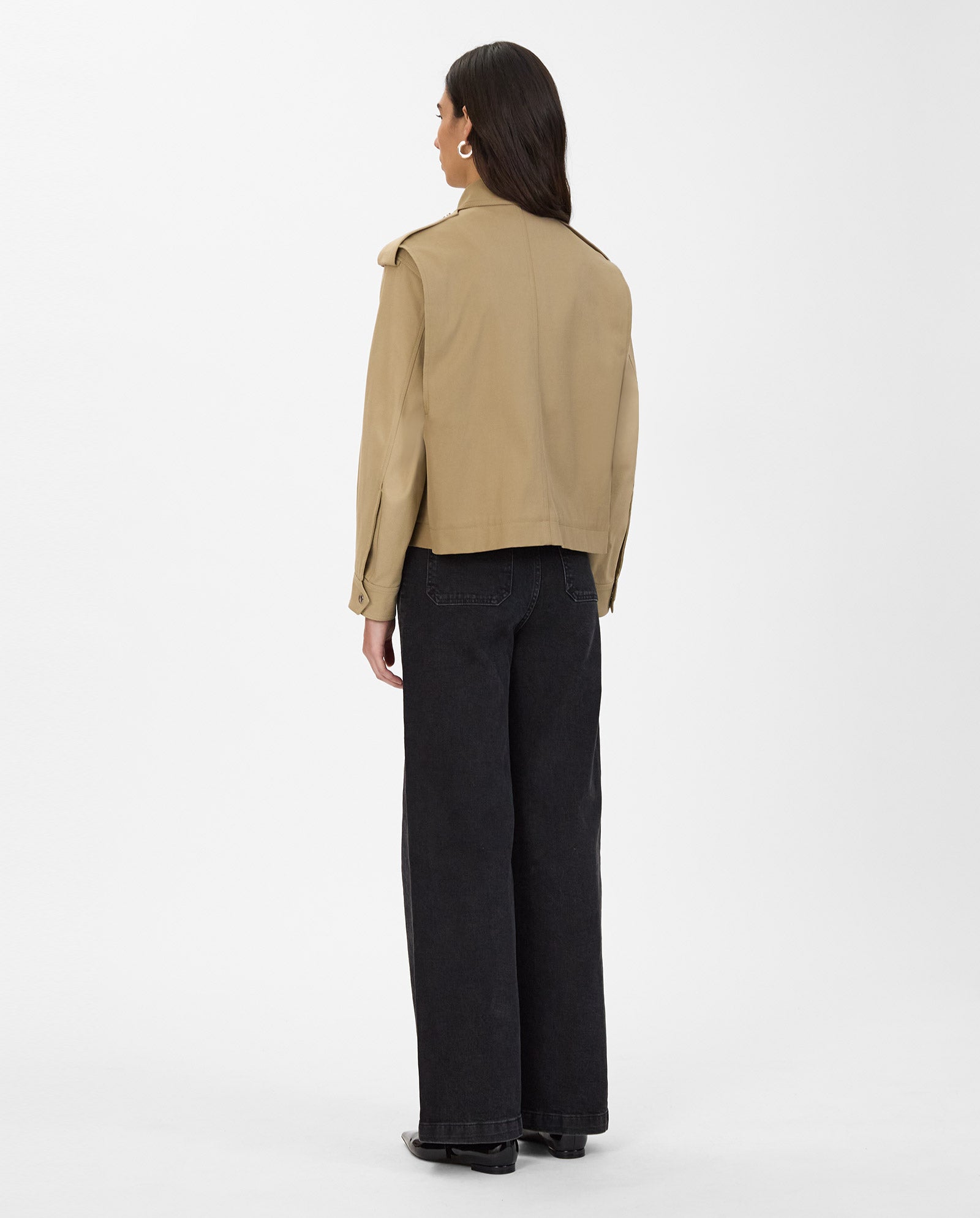 A woman stands with her back to the camera, wearing the IVY OAK JOANNE Jacket in tan with yoke flaps and wide-leg black jeans, set against a white background.