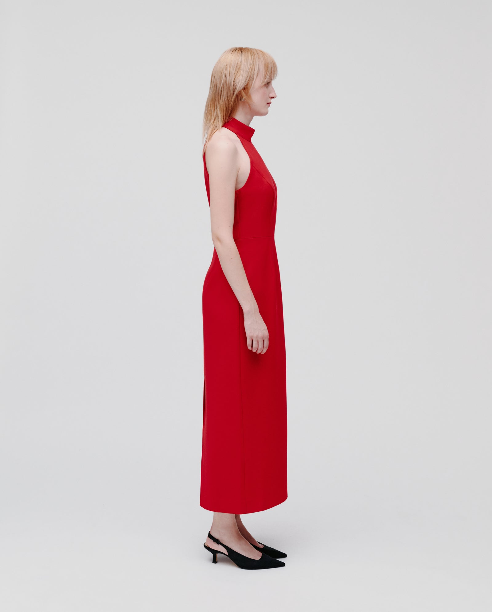 A person in a body-hugging, sleeveless red IVY OAK NOLAN Dress and black heels stands in profile against a plain white background.
