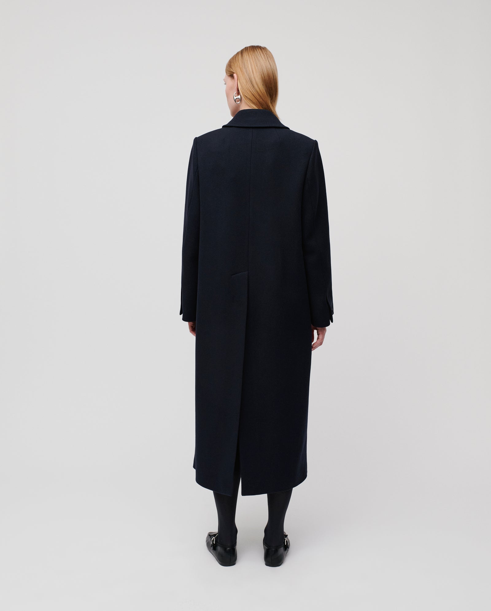 A person with straight blond hair is seen from the back wearing the IVY OAK CLEMENCE Coat, styled with black tights and shoes.