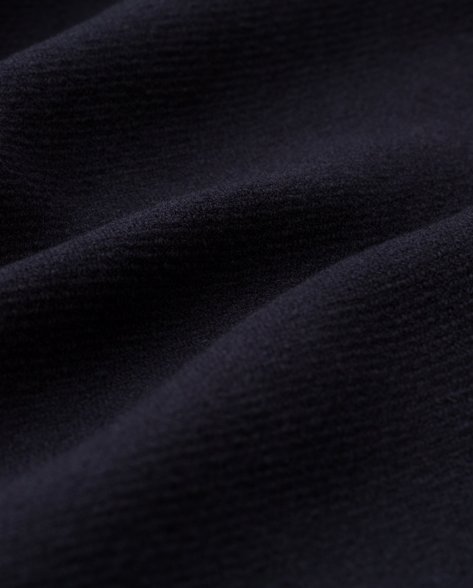 Close-up of the dark, textured fabric of the CLEMENCE Coat by IVY OAK, featuring soft folds and a subtle play of light and shadow.