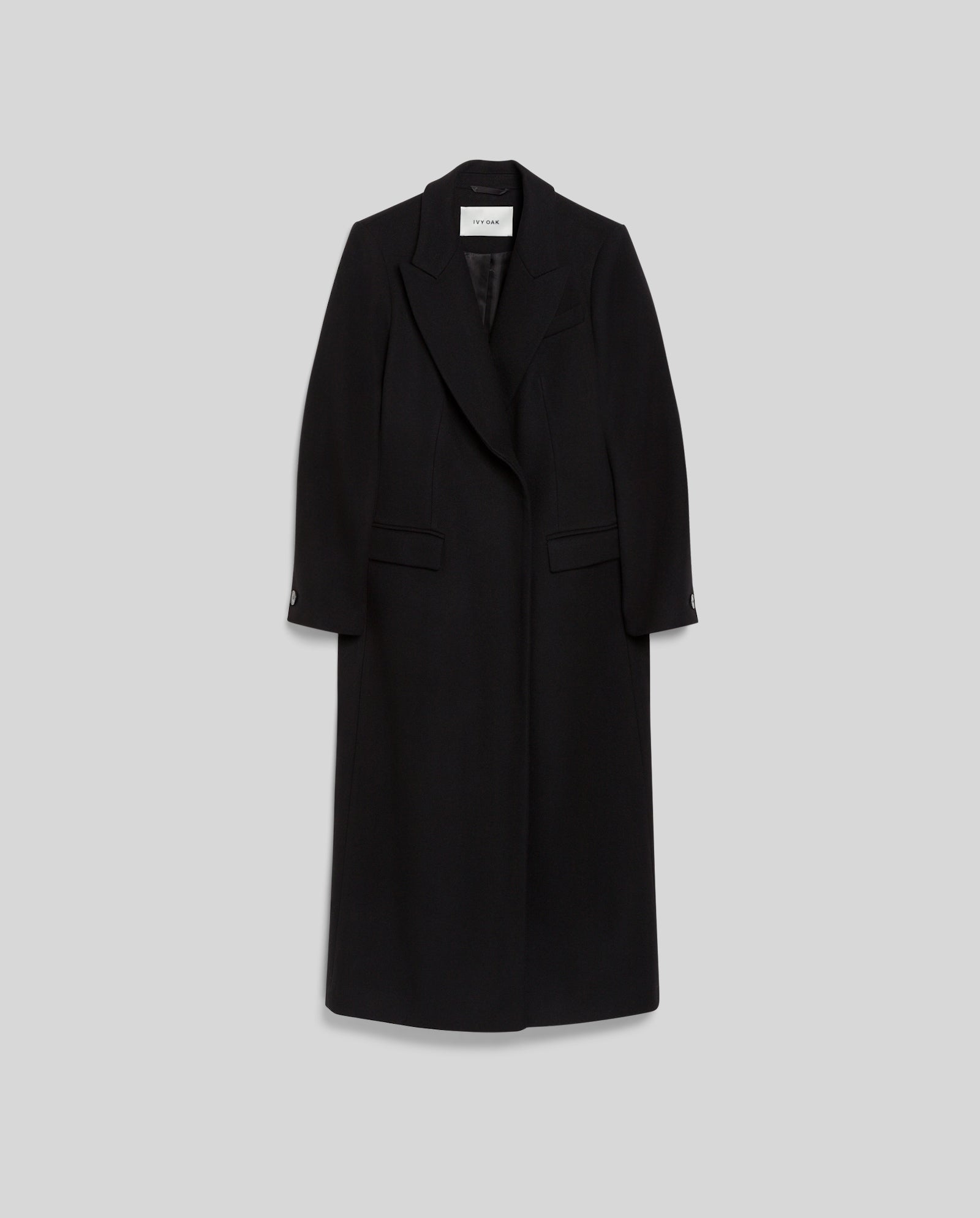The CYNTHIA Coat by IVY OAK is a long black virgin wool coat with lapels, two front pockets, and a fitted waist, shown against a plain light gray background.