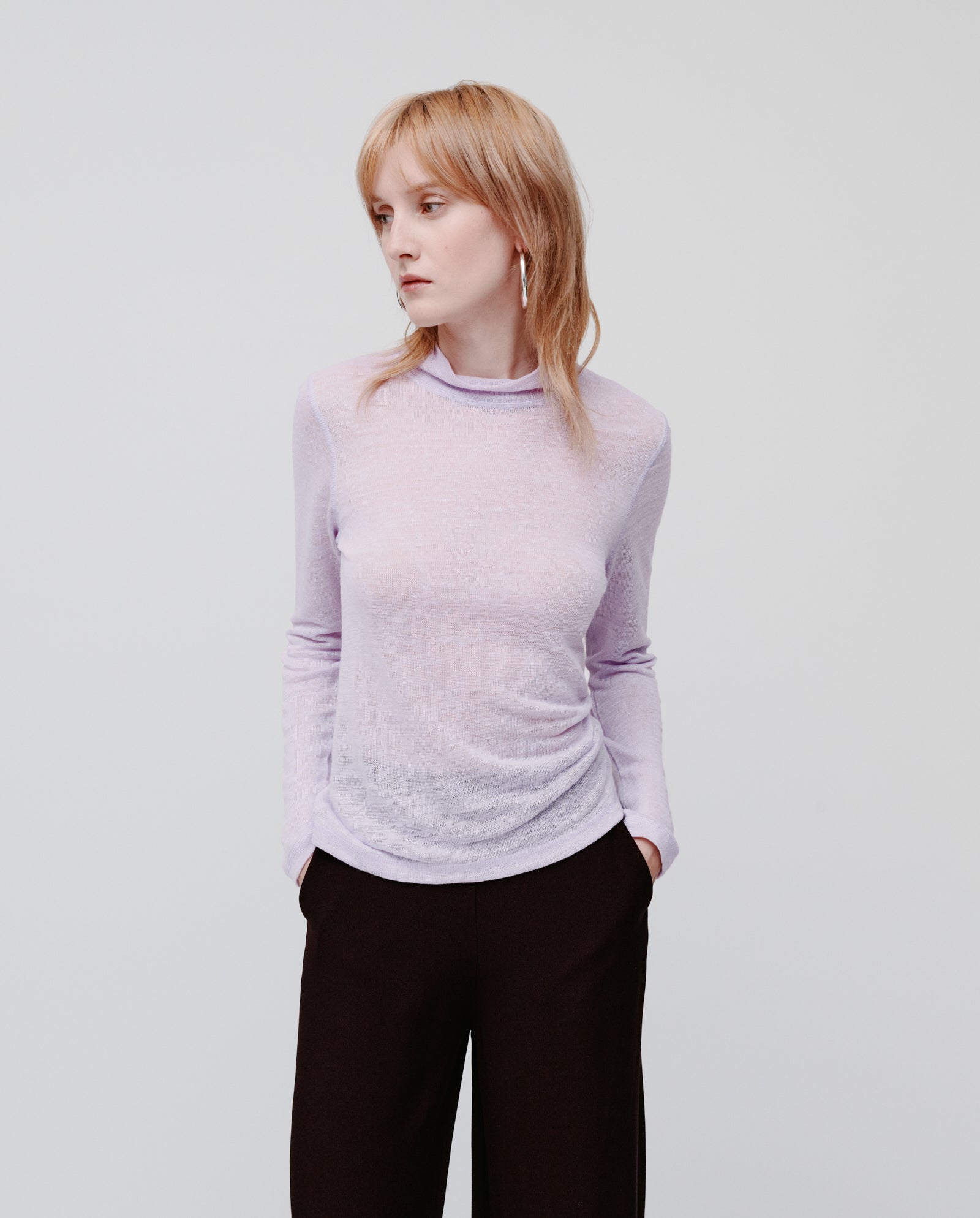 Woman in an IVY OAK FELINE Top in light purple and black pants stands with hands in pockets, looking to the side.