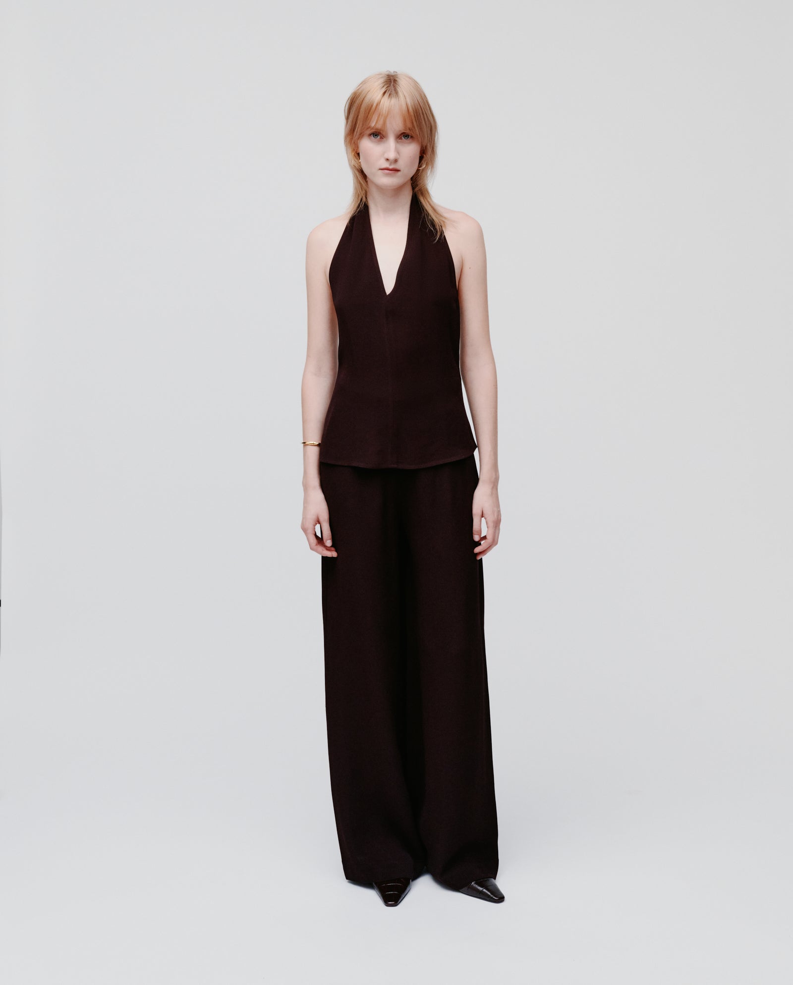 A woman wears the IVY OAK TANSY Top, a sleeveless black neckholder, paired with wide-leg black crepe pants, standing against a plain white background.