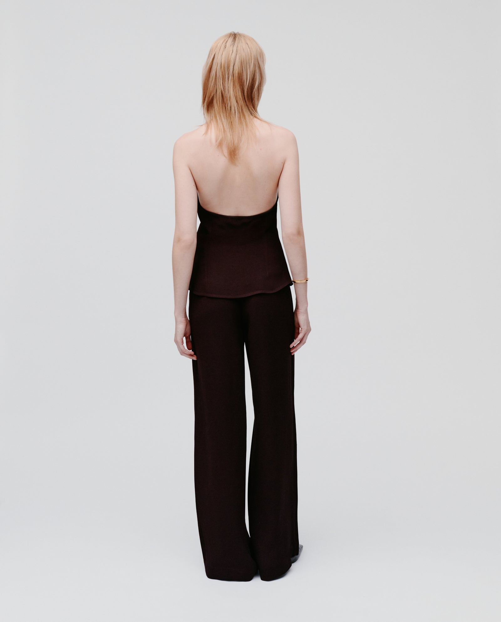 A blonde woman, facing away against a plain light background, wears the IVY OAK TANSY Top made from black crepe fabric.