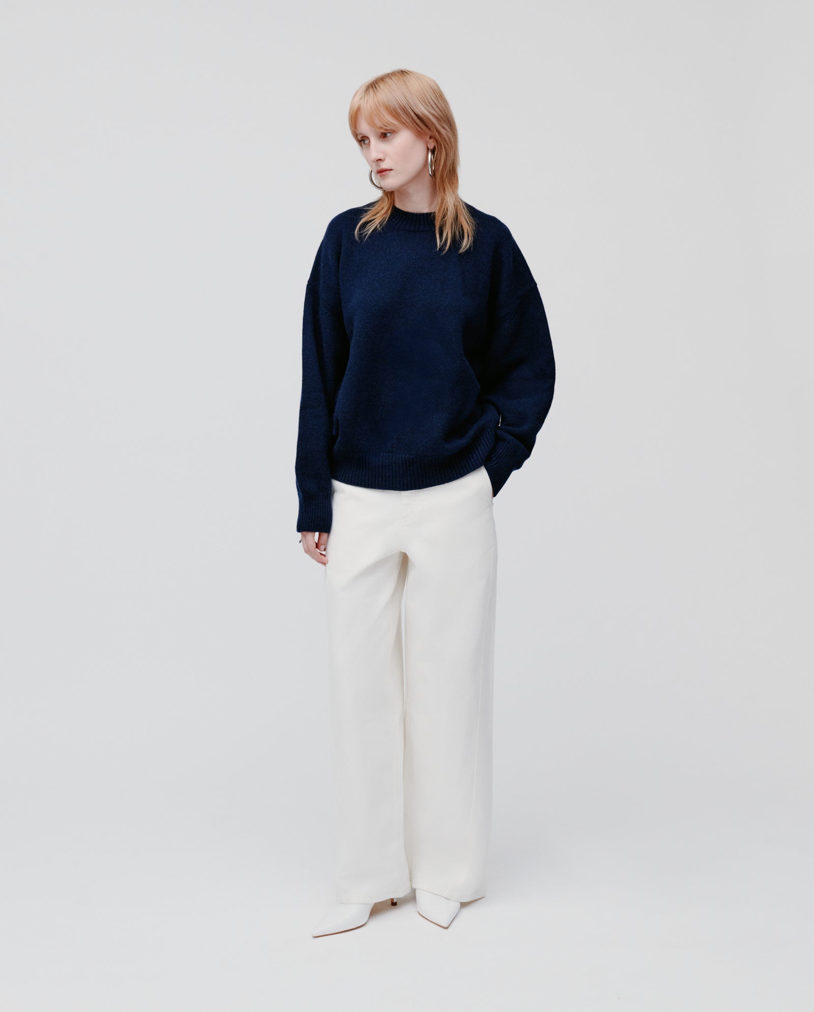 A person wearing the IVY OAK KASSIDY Jumper in navy, paired with white wide-leg pants and white shoes, stands against a plain light background.