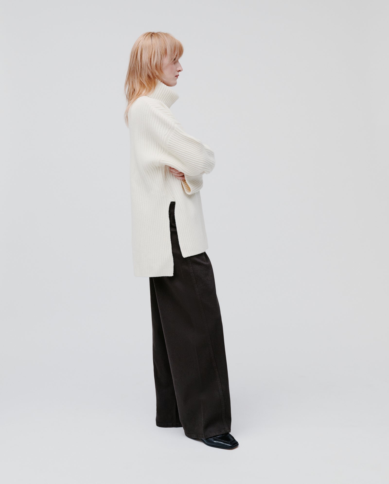 A person stands in profile against a white background wearing the IVY OAK KYOMI ANN Jumper and black wide-leg pants.