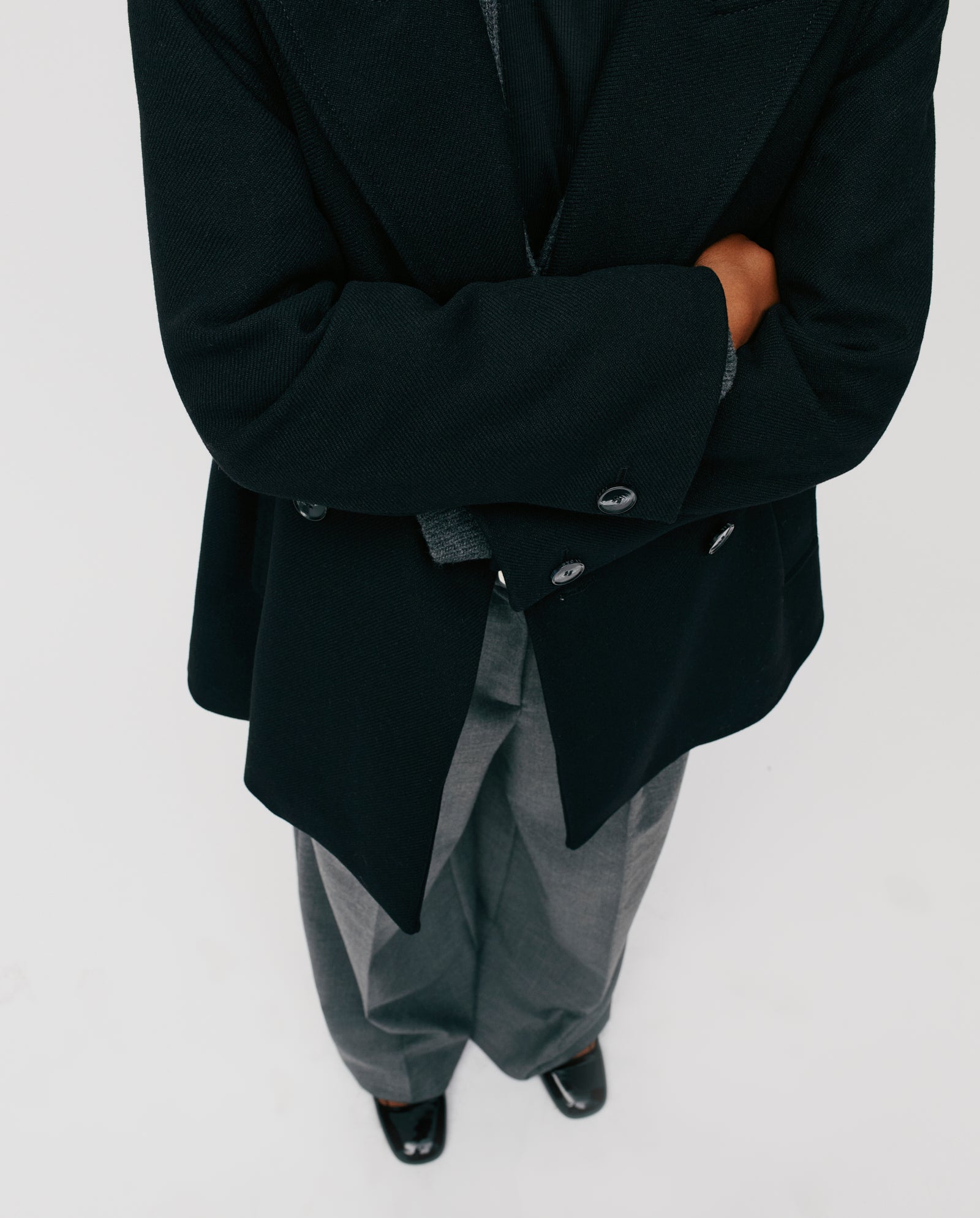 A person stands with arms crossed, viewed from above against a white background, wearing the IVY OAK JENNA Jacket styled with gray pants.