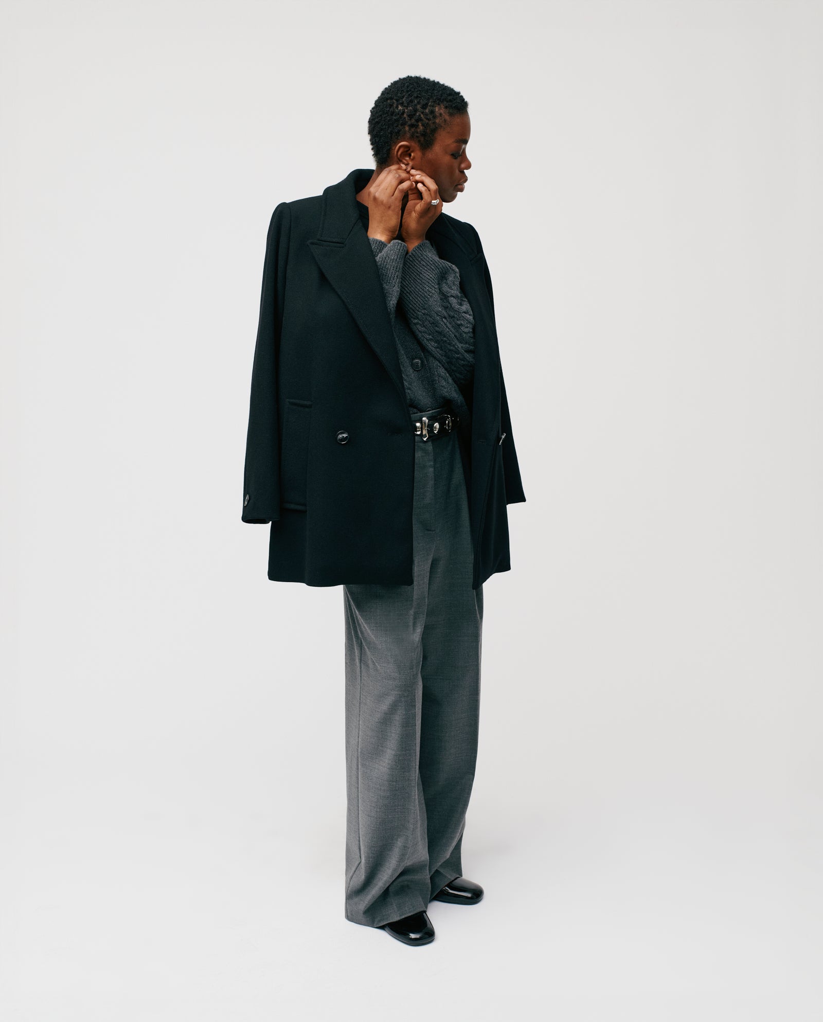 A person wearing the IVY OAK JENNA Jacket in black over a grey sweater and gray wide-leg pants, looking to the side.