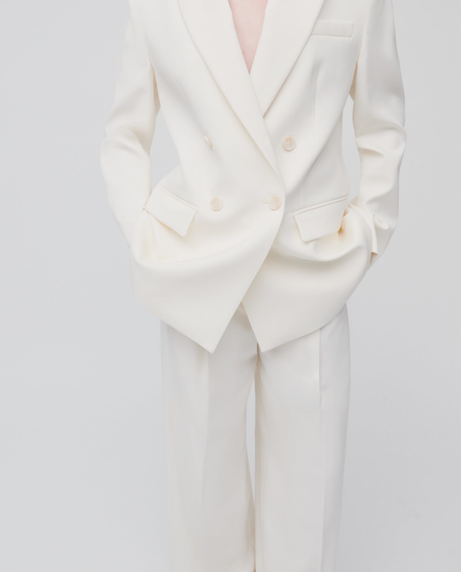 A person wears the IVY OAK JUDITH Blazer, a double-breasted white suit, with hands in pockets against a plain light background.